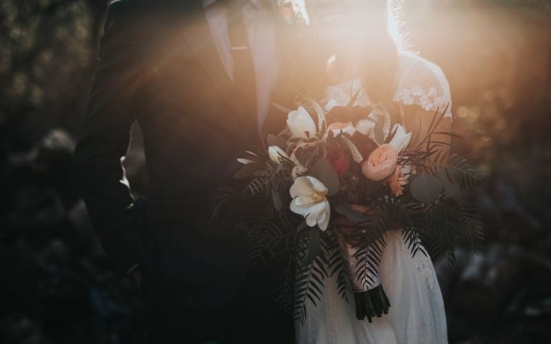 Young bride and groom with a dark background and bright sunlight coming over their shoulders.