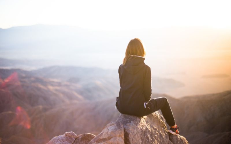 View of a woman from the back, sitting on top of a mountain looking out at the view