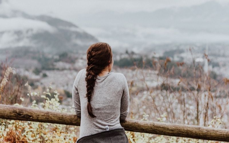 woman leaning against fence, looking out over snowy fields and mountains