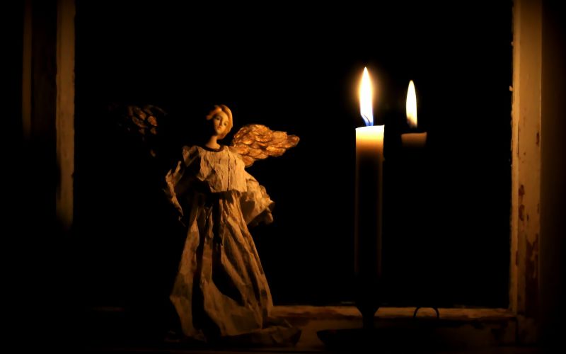 Christmas angel figure in a dark window next to a candle