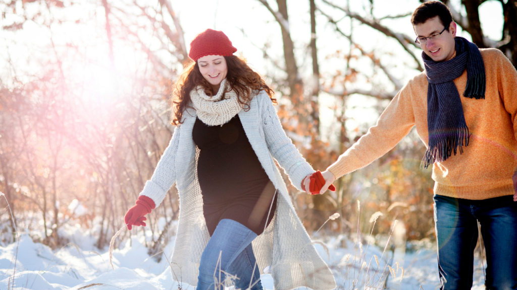 married couple holding hands walking through snowy woods