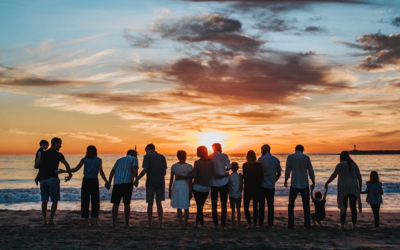 large family on beach at sunset, photo taken from behind