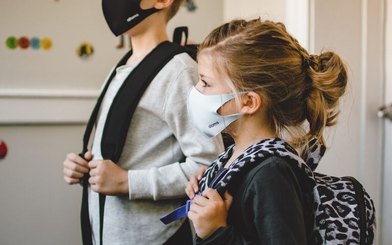 two schoolchildren carrying backpacks and wearing masks