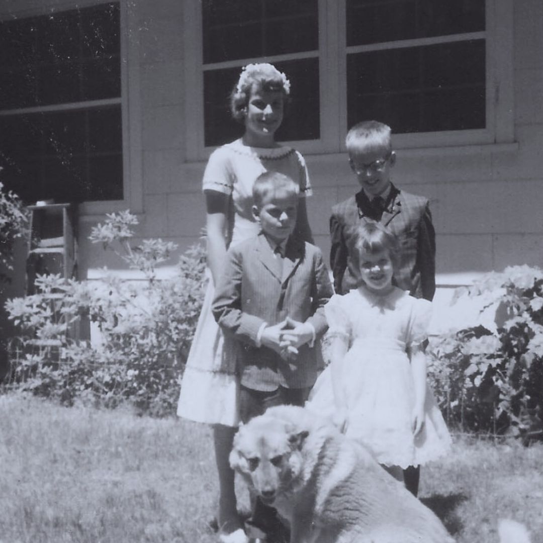 Black and white photo with four children and a dog, in the front yard with house behind them.