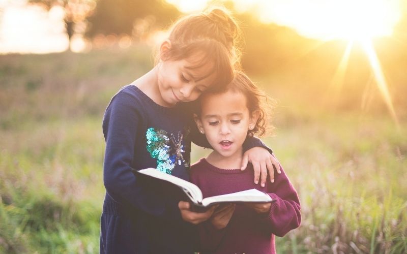 two small children in a field, reading a Bible