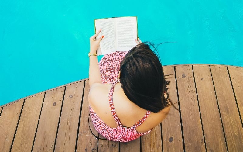 Woman sitting by a pool reading a book.